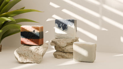 Decorative items including a rectangular object, a cylindrical container, and a square object on a light surface with a plant in the corner.